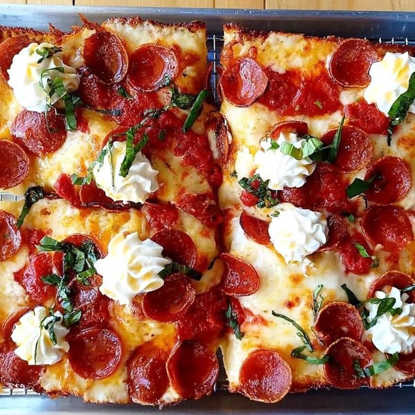 Two rectangular slices of Sodough Square pepperoni pizza with dollops of white cheese and fresh basil.