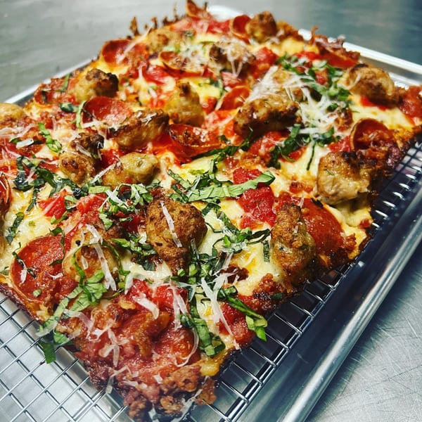 A square Sodough Square pizza with pepperoni, sausage, basil, and cheese on a cooling rack.