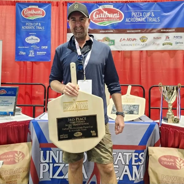 A man from Sodough Square holds a 3rd place award from the Galbani Pizza Cup & Acrobatic Trials.