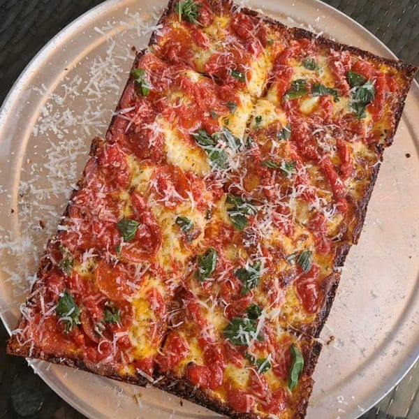 A rectangular Sodough Square pizza with red sauce, melted cheese, basil, and grated parmesan.
