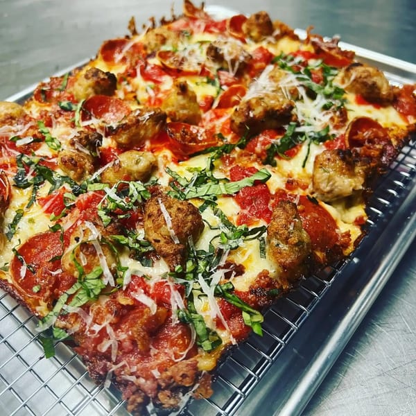 Sodough Square pizza with pepperoni, sausage, basil, and parmesan on a metal cooling rack.