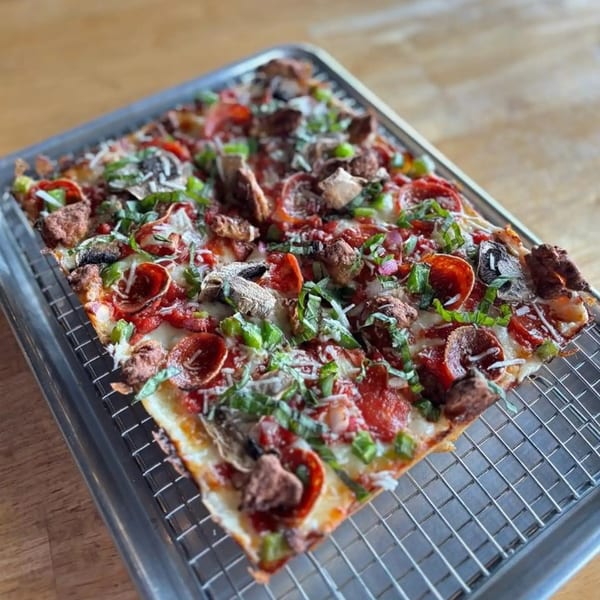 A rectangular Sodough Square pizza with pepperoni, mushrooms, sausage, and green herbs on a metal tray.