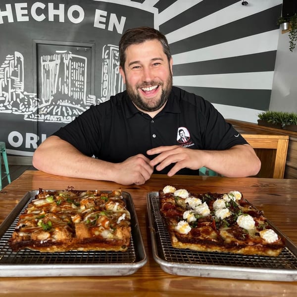 Smiling man behind two Sodough Square pizzas, one with chicken, the other with ricotta.