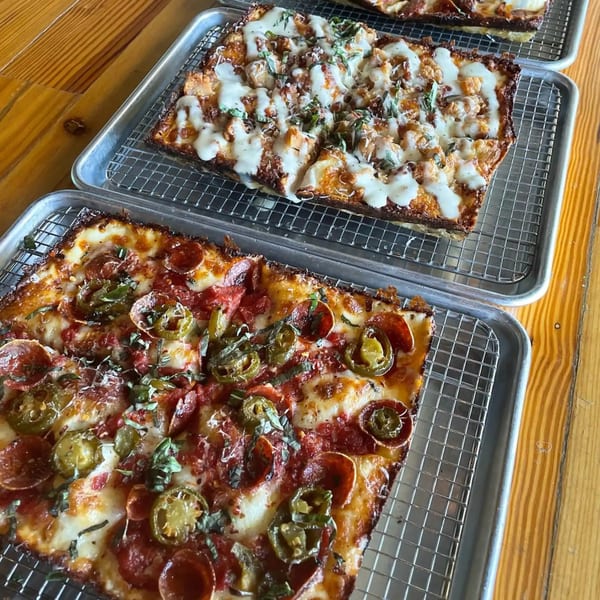 Two rectangular Sodough Square pizzas on metal cooling racks, one with pepperoni and jalapeños.