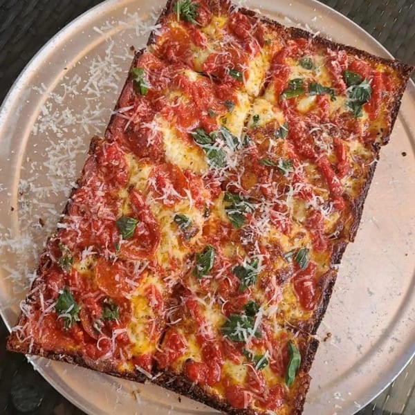 A rectangular Sodough Square pizza with red sauce, melted cheese, basil, and grated parmesan.