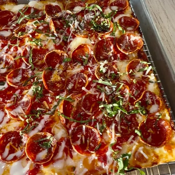 Close-up of a rectangular Sodough Square pepperoni pizza with melted cheese, fresh basil, and grated parmesan.