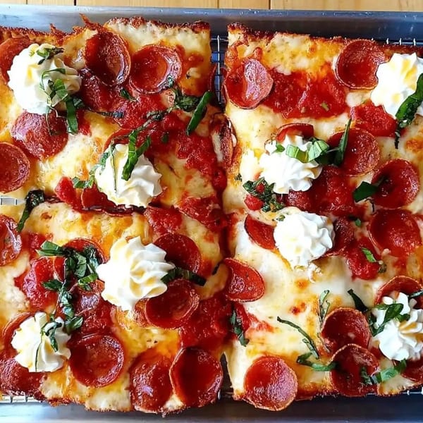 Two square slices of Sodough Square pepperoni pizza with dollops of ricotta and fresh basil.