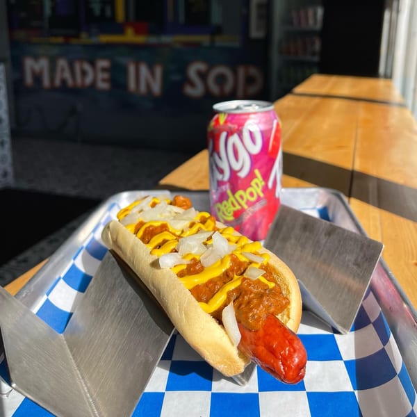 A chili cheese hot dog with diced onions and mustard, next to a pink Faygo Redpop can.